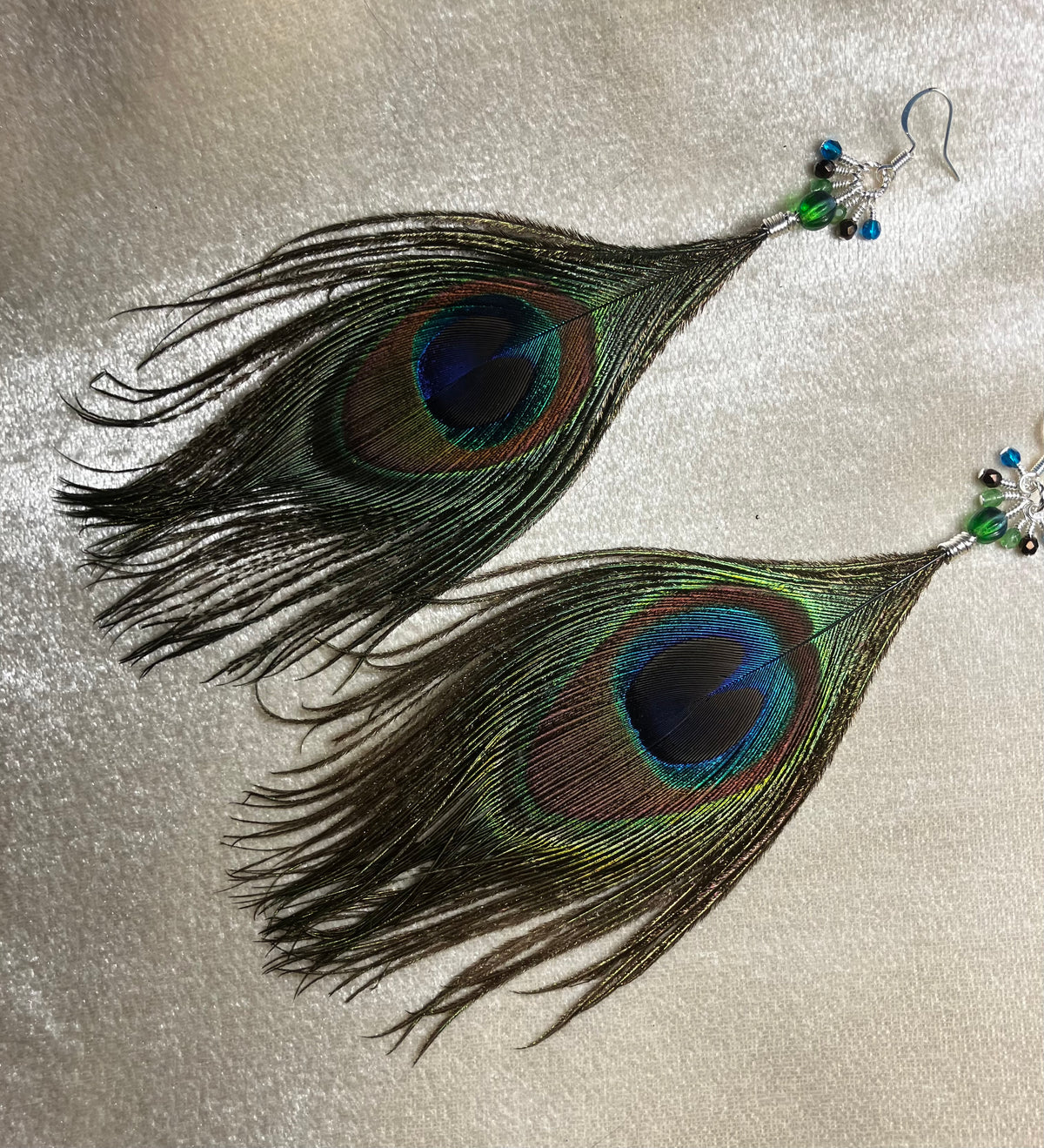 Peacock eye feather earrings adorned with small dangling green, brown, and teal Czech glass beads.