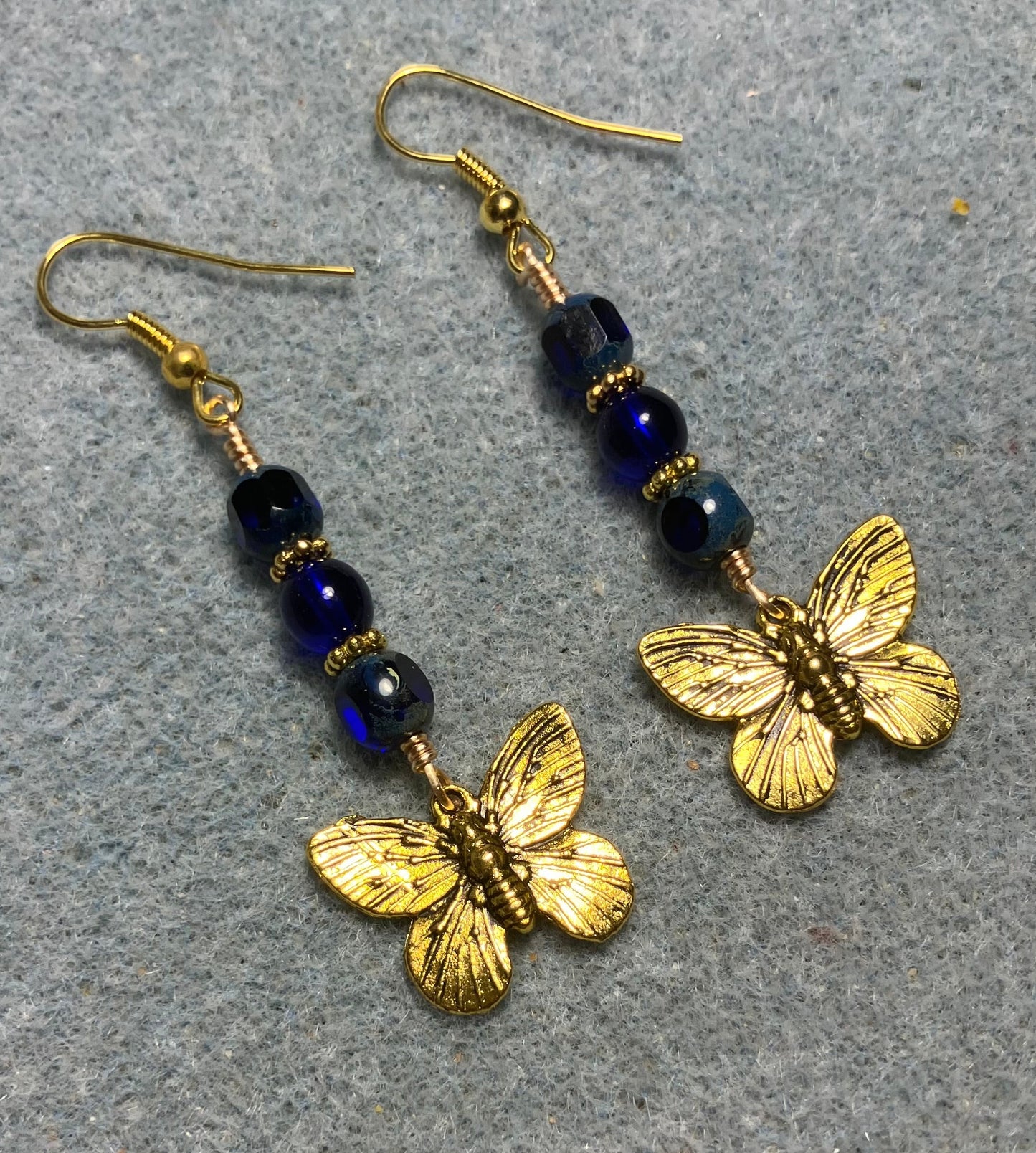 Gold butterfly charm earrings adorned with cobalt blue Czech glass beads.