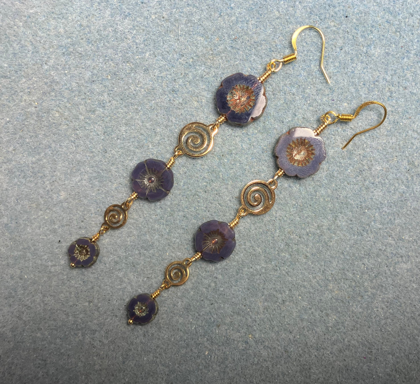 Extra long purple flower bead earrings made with three sizes of purple Czech glass pansy beads joined by gold swirly connectors.