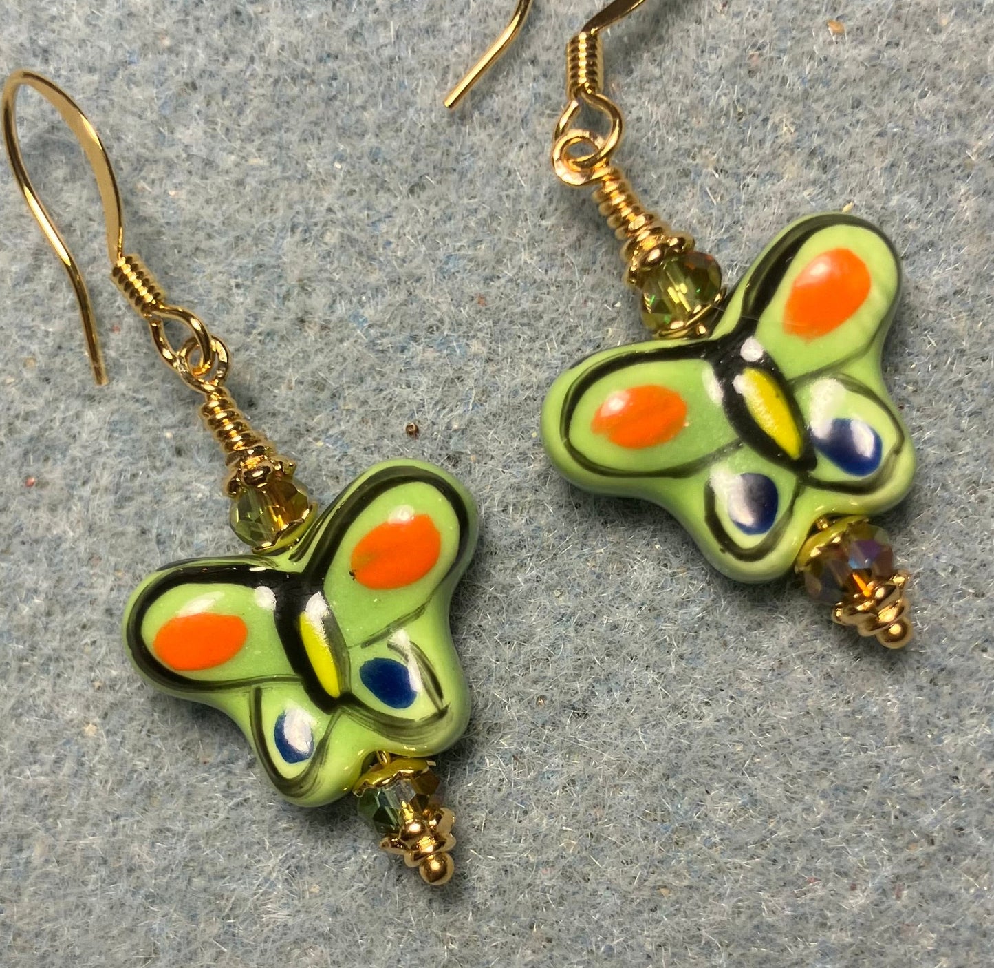 Olive green and orange ceramic butterfly bead earrings adorned with sparkly olive green Chinese crystal beads.