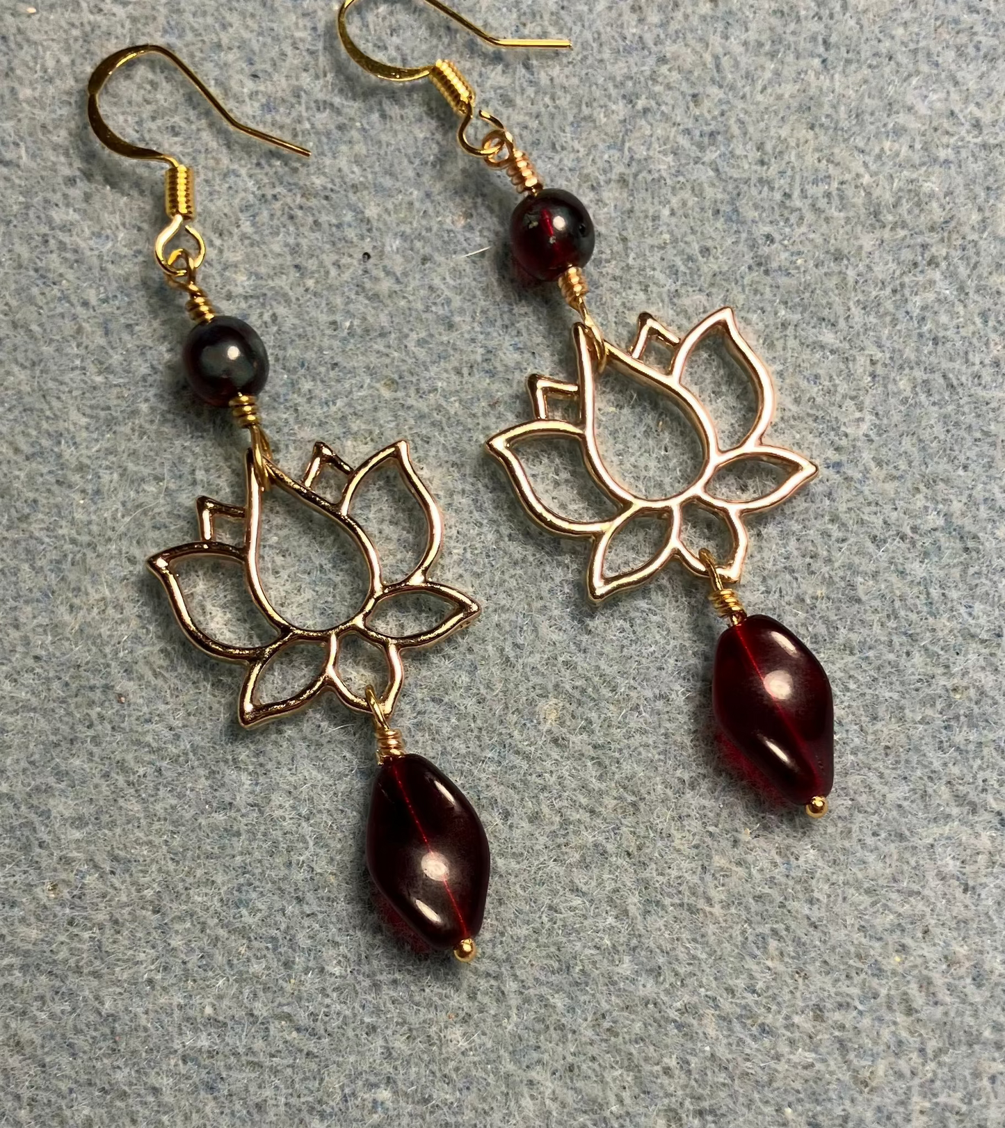 Gold lotus flower connector charm earrings adorned with dark red Czech glass twist beads and dark red Czech glass beads.